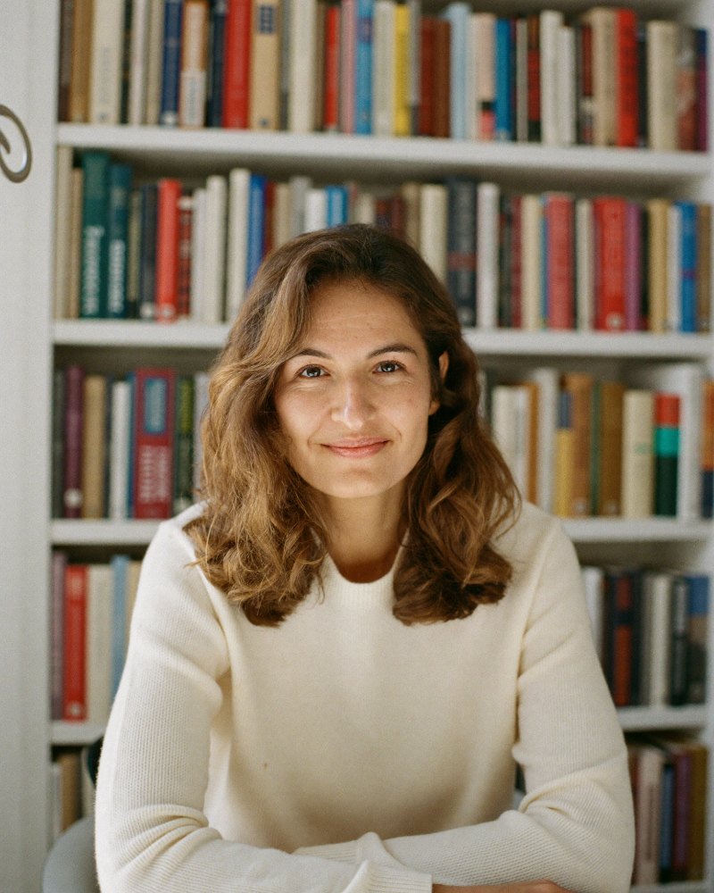 A romance novelist at her home office bookshelf
